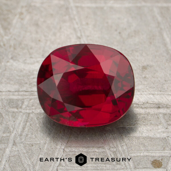 2.27-Carat Mozambique Ruby (Heated) A 2.27-carat heated Mozambique ruby, cut in a faceted oval shape, is displayed on a textured metallic surface above the text "EARTH'S TREASURY.