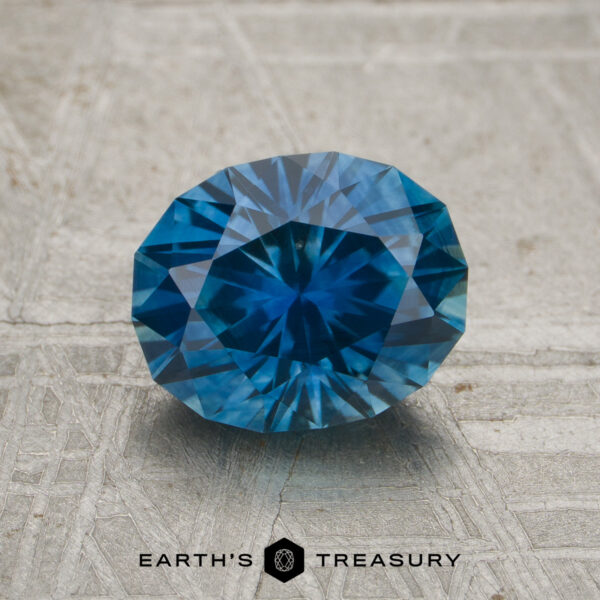 1.83-Carat Rich Blue Montana Sapphire (Heated) A 1.83-carat rich blue Montana sapphire (heated), cut in an oval facet, is displayed on a textured gray surface with the words "EARTH'S TREASURY" at the bottom.