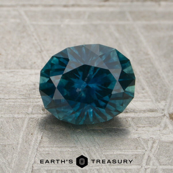 A 1.78-carat Deep Peacock Montana Sapphire (Heated) is showcased on a textured light surface, with the Earth's Treasury logo and text visible at the bottom.
