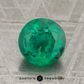 A 1.65-carat rich green Zambian emerald, precision round-cut, rests on a textured gray surface with the text "Earth's Treasury" at the bottom.