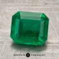 A 2.56-carat rich green Zambian emerald, cut in a rectangular shape, is displayed on a textured surface with the Earth’s Treasury logo beneath it.