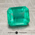 A 2.45-carat bright green Brazilian emerald with an emerald cut sits on a textured surface. The words "EARTH'S TREASURY" and a hexagon logo appear at the bottom of the image.
