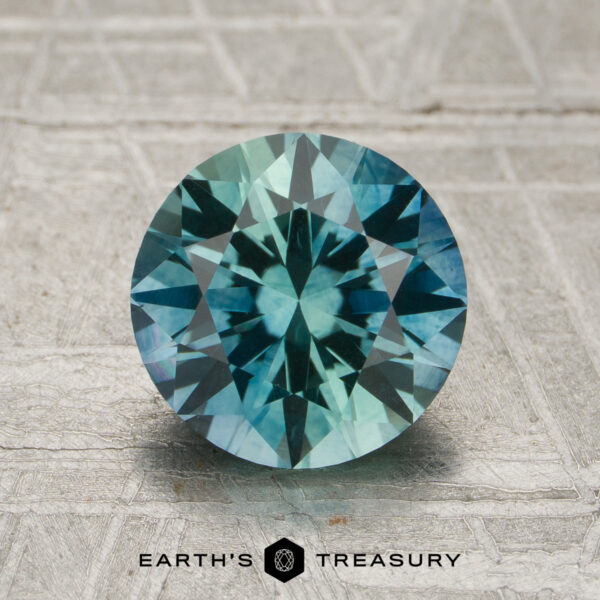 2.17-Carat Aqua Blue-Green Particolored Montana Sapphire (Heated 2.17-carat aqua blue-green particolored Montana sapphire (heated), round brilliant-cut, displayed on a textured gray background with the "Earth's Treasury" logo at the bottom.