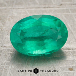 3.19-carat bright green Zambian emerald, oval-cut, displayed on a textured gray surface with the "EARTH'S TREASURY" logo at the bottom.