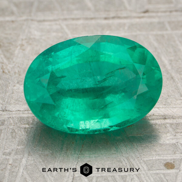 3.19-Carat Bright Green Zambian Emerald 3.19-carat bright green Zambian emerald, oval-cut, displayed on a textured gray surface with the "EARTH'S TREASURY" logo at the bottom.