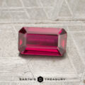 A rectangular, faceted 1.02-carat Mozambique ruby (heated) is displayed on a textured gray surface, with the text "EARTH'S TREASURY" at the bottom of the image.