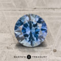Certainly! Here is the rewritten sentence using the provided product data: A 1.71-carat teal to violet blue color-change Montana sapphire in a round brilliant cut is displayed on a textured gray surface, with the "Earth's Treasury" text and logo positioned beneath.