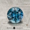 A 1.71-carat teal to violet blue color-change Montana sapphire, cut in a round brilliant style, is displayed on a textured surface. The Earth's Treasury logo and name appear at the bottom of the image.