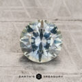 A round, faceted 1.66-carat Montana sapphire, exhibiting aqua to steely blue-gray color-change hues, is displayed on a textured surface. "EARTH'S TREASURY" is written at the bottom of the image.