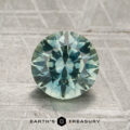A 1.66-carat aqua to steely blue-gray color-change Montana sapphire, cut into a round, faceted shape, is displayed upright on a textured surface with the words "Earth's Treasury" below it.