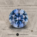 A 1.61-carat teal blue to purple color-change Montana sapphire (Heated) in a round brilliant cut displayed on a textured surface, with the "Earth's Treasury" logo and text at the bottom of the image.