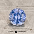 A 1.55-carat medium blue to purple color-change Montana sapphire, expertly cut in a round brilliant style, rests on a textured gray surface. The words "Earth's Treasury" and a hexagon logo are displayed at the bottom of the image.