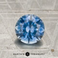 A round, faceted 1.55-carat medium blue to purple color-change Montana sapphire is displayed on a textured silver surface, with the "Earth's Treasury" logo and text at the bottom.