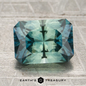 A 2.48-carat aqua green-teal particolored Montana sapphire (heated), cut in a rectangular emerald shape, is displayed on a textured surface featuring the "Earth's Treasury" logo at the bottom.