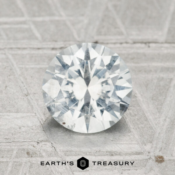 1.58-Carat Montana Sapphire A 1.58-carat Montana sapphire is displayed on a textured gray surface, with "EARTH'S TREASURY" and a geometric logo visible at the bottom.