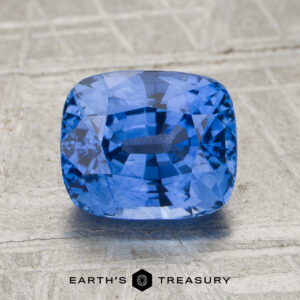 2.40-carat cornflower blue Ceylon sapphire (heated) in a cushion cut, showcased on a textured surface with the "Earth's Treasury" logo at the bottom.