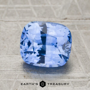 A 2.37-carat sky blue Ceylon sapphire (heated), faceted in a cushion cut, is displayed on a textured light surface with the "Earth's Treasury" logo at the bottom of the image.