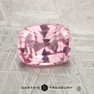 A cushion-cut pink gemstone, product JM-001-398JM-G, rests on a textured gray surface with the "Earth's Treasury" logo below.