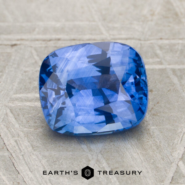 2.52-Carat Ceylon Sapphire (Heated) A 2.52-carat heated Ceylon sapphire with a cushion cut rests on a textured light gray surface, with the Earth's Treasury logo at the bottom.