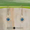 Stacked from 16 images using Method=B (R=7, S=2), these gold drop earrings feature blue center gemstones with white accent stones and are displayed hanging from a green leaf. The "EARTH'S TREASURY" logo and text appear at the bottom of the image.