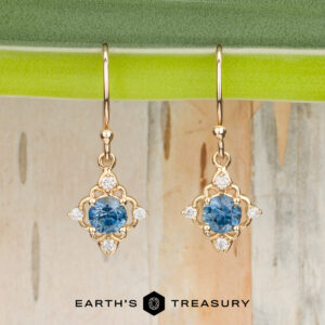 Stacked from 18 images using Method=B (R=7, S=2), these gold drop earrings with blue gemstones and small diamonds are displayed hanging from a green leaf, with the "Earth's Treasury" logo and name featured at the bottom.