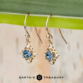 Stacked from 20 images (Method=B, R=7, S=2) gold drop earrings with blue gemstones and small clear stones are displayed hanging from a green leaf. The Earth's Treasury logo and name appear at the bottom of the image.