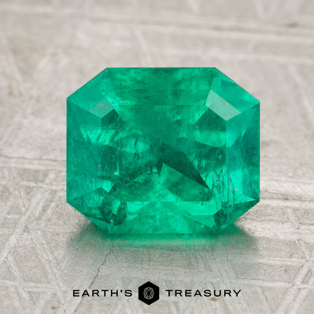 A rectangular step-cut green emerald gemstone, JV-001-758H, is showcased on a textured surface with the "Earth's Treasury" logo below—offering a stunning example for any Emerald Guide.