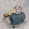 The "Eden" Halo Ring featuring an oval pink gemstone with white accent stones, displayed on a rough blue crystal with Earth’s Treasury logo beneath.