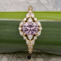 The "Eden" Halo Ring featuring a round lavender gemstone at the center, accented by marquise and round white diamonds, displayed on a green leaf.