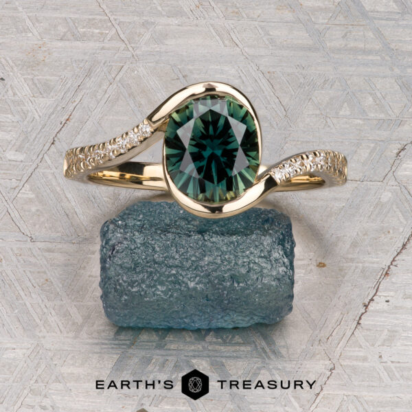 The "Cara" ring The "Cara" ring featuring an oval green gemstone and small side diamonds, displayed on a rough blue-green crystal with the “Earth’s Treasury” logo below.