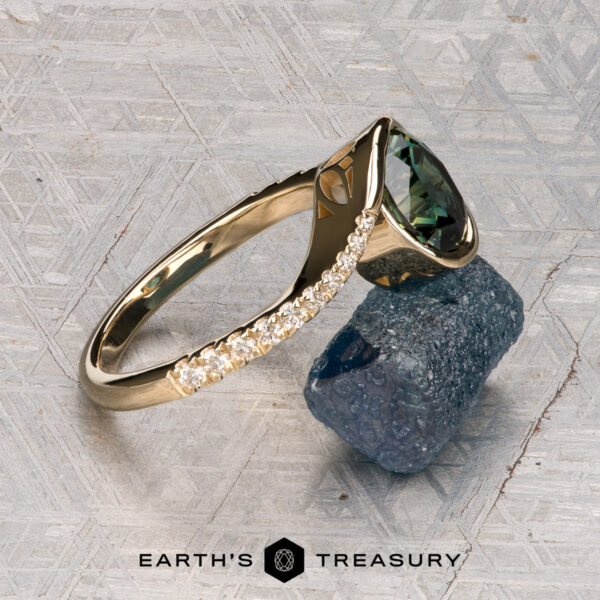 The "Cara" ring The "Cara" ring, featuring a green gemstone and small diamonds, is displayed on a rough dark blue mineral against a textured gray background. The words “EARTH’S TREASURY” are shown at the bottom.