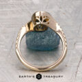 The "Cara" ring is displayed upright on a rough blue stone, featuring a decorative top with a patterned surface and the Earth’s Treasury logo beneath.