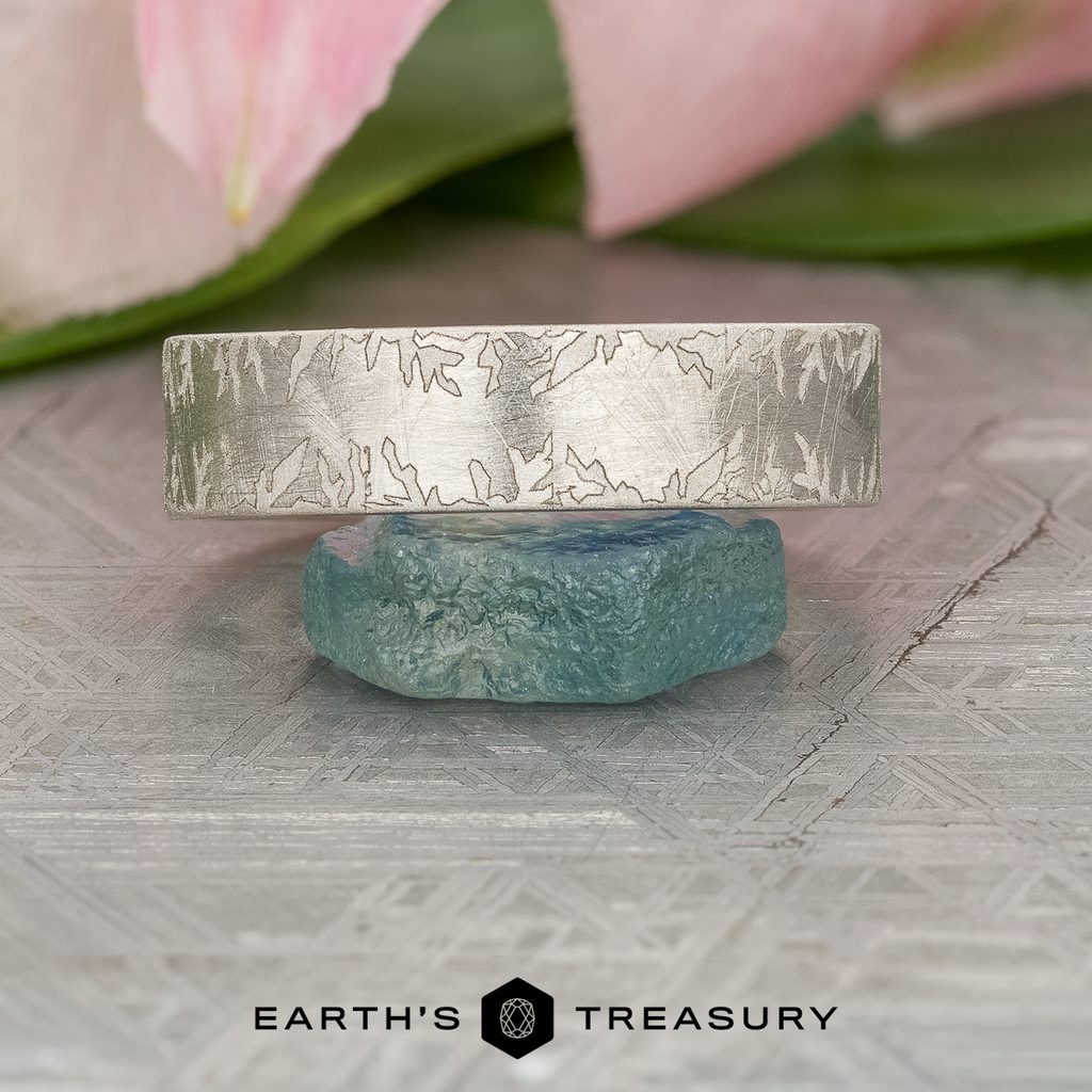 A silver ring with intricate engravings rests on a blue-green stone, its textured pattern catching the light. In the background, a blurred pink flower adds a soft touch. Text at the bottom reads “Stacked from 16 images. Method=B (R=14,S=2).”.
