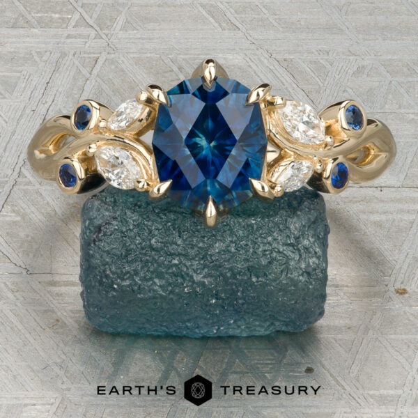The "Althea" Ring in 14K yellow gold featuring a 1.89-Carat Royal Blue Montana Sapphire (Heated) Gold ring “Althea” featuring an oval blue gemstone, marquise and round clear stones, and delicate blue accents, showcased on a rough blue crystal.