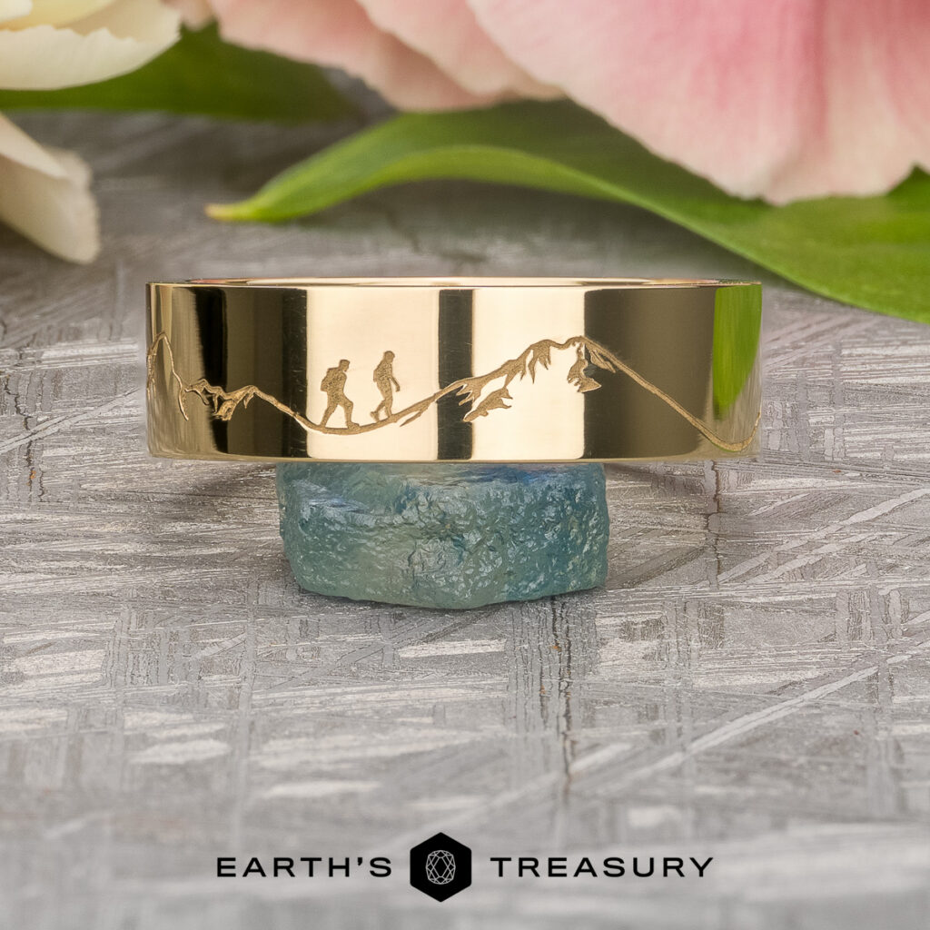 Stacked from 15 images using Method=B (R=7, S=2), this gold ring features intricate engravings of hikers and a mountain range, displayed atop a blue gemstone with the Earth’s Treasury logo visible below.
