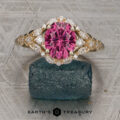 The "Eden" Halo Ring featuring an oval pink gemstone and marquise diamonds, displayed upright on a textured dark stone with the Earth’s Treasury logo visible at the bottom of the image.