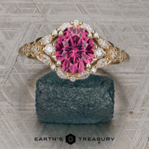 The "Eden" Halo Ring featuring an oval pink gemstone and marquise diamonds, displayed upright on a textured dark stone with the Earth’s Treasury logo visible at the bottom of the image.