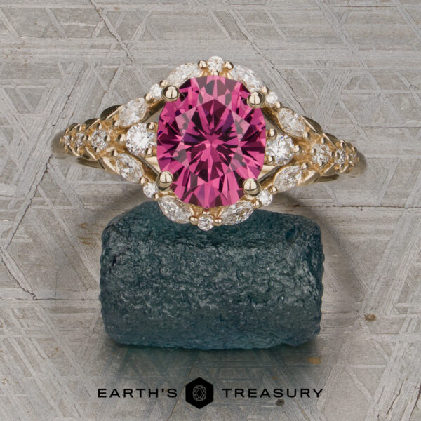 The "Eden" Halo Ring in 14K yellow gold with a 2.20ct rose pink garnet. The "Eden" Halo Ring featuring an oval pink gemstone and marquise diamonds, displayed upright on a textured dark stone with the Earth’s Treasury logo visible at the bottom of the image.