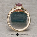 The "Eden" Halo Ring with a pink gemstone is displayed upright on a rough blue stone, with the Earth’s Treasury logo below on a textured surface.