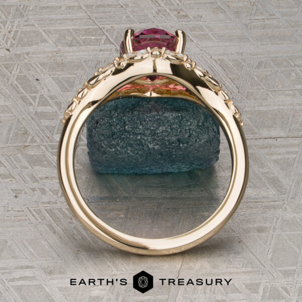The "Eden" Halo Ring in 14K yellow gold with a 2.20ct rose pink garnet. The "Eden" Halo Ring with a pink gemstone is displayed upright on a rough blue stone, with the Earth’s Treasury logo below on a textured surface.