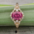 The "Eden" Halo Ring, featuring a round pink gemstone at the center surrounded by small clear stones, displayed on a green patterned surface with “Earth’s Treasury” at the bottom.
