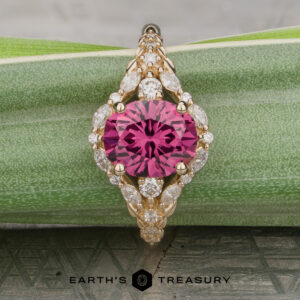 The "Eden" Halo Ring, featuring a round pink gemstone at the center surrounded by small clear stones, displayed on a green patterned surface with “Earth’s Treasury” at the bottom.
