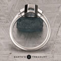 The "Everly" Three-Stone Ring in Platinum 950 with a 1.83-Carat Peacock Blue Montana Sapphire (Heated)—is displayed upright on a textured surface, with “EARTH’S TREASURY” and a geometric logo at the bottom.