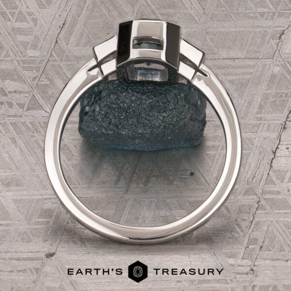 The "Everly" Three-Stone Ring in Platinum 950 with a 1.83-Carat Peacock Blue Montana Sapphire (Heated) The "Everly" Three-Stone Ring in Platinum 950 with a 1.83-Carat Peacock Blue Montana Sapphire (Heated)—is displayed upright on a textured surface, with “EARTH’S TREASURY” and a geometric logo at the bottom.