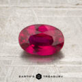 A 1.10-carat heated Thai ruby, cut in an oval shape, rests on a textured gray surface. The text “EARTH’S TREASURY” appears at the bottom of the image.