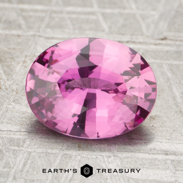 A 2.63-carat heated pink sapphire, cut in an oval shape, rests on a textured surface with the words “Earth’s Treasury” at the bottom of the image.