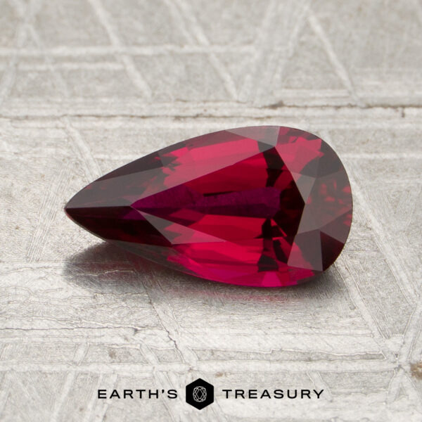 1.31-Carat Mozambique Ruby (Heated) A faceted, pear-shaped 1.31-carat Mozambique Ruby (heated) in deep red rests on a textured, metallic surface with the “Earth’s Treasury” logo at the bottom.