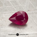 A pear-shaped, faceted 0.86-carat Burmese ruby (heated) is displayed on a textured surface with the logo and text “Earth’s Treasury” at the bottom.