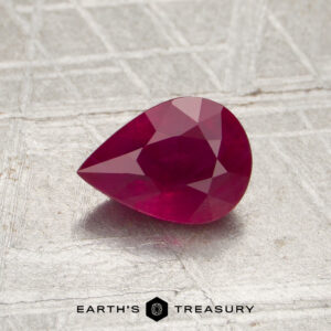 A pear-shaped, faceted 0.86-carat Burmese ruby (heated) is displayed on a textured surface with the logo and text “Earth’s Treasury” at the bottom.
