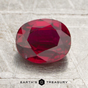 A 1.29-carat Mozambique Ruby (heated), faceted in an oval shape, rests on a textured silver surface, with the Earth’s Treasury logo and text below.